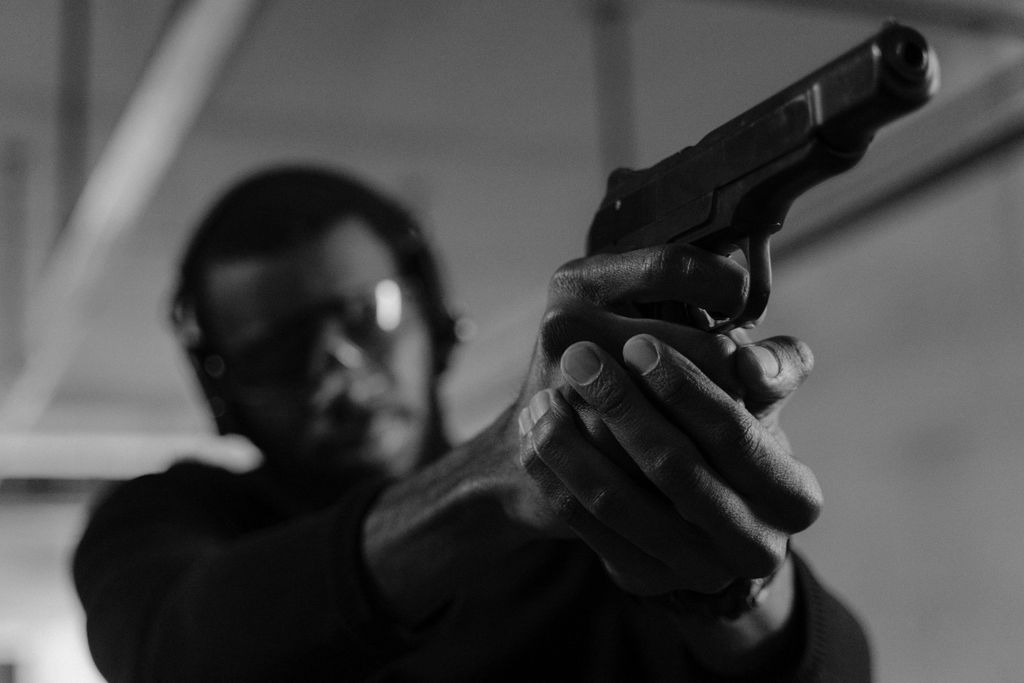 Black and white photo of a man aiming a handgun at an indoor shooting range.