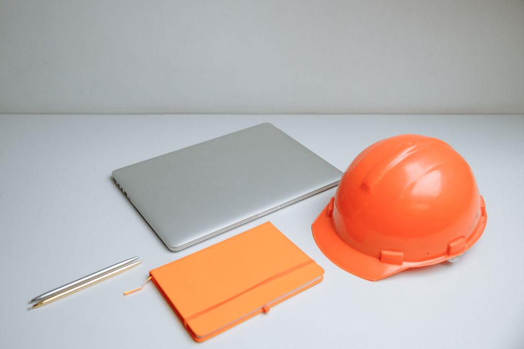 Sleek desk setup featuring a laptop, notebook, and orange hardhat.